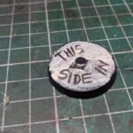 A magnet key on a cutting mat. The top of the round metal reads 'This side in' in handwriting