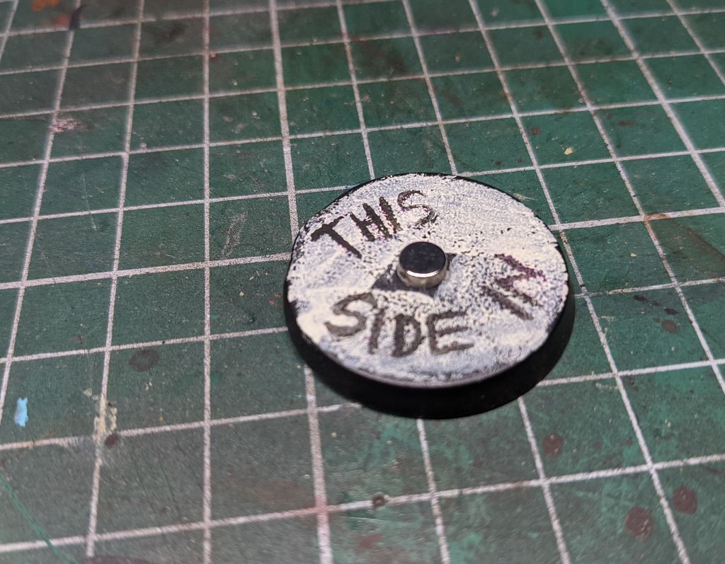 A magnet glued to a model base. 'This side in' is written on the front.
