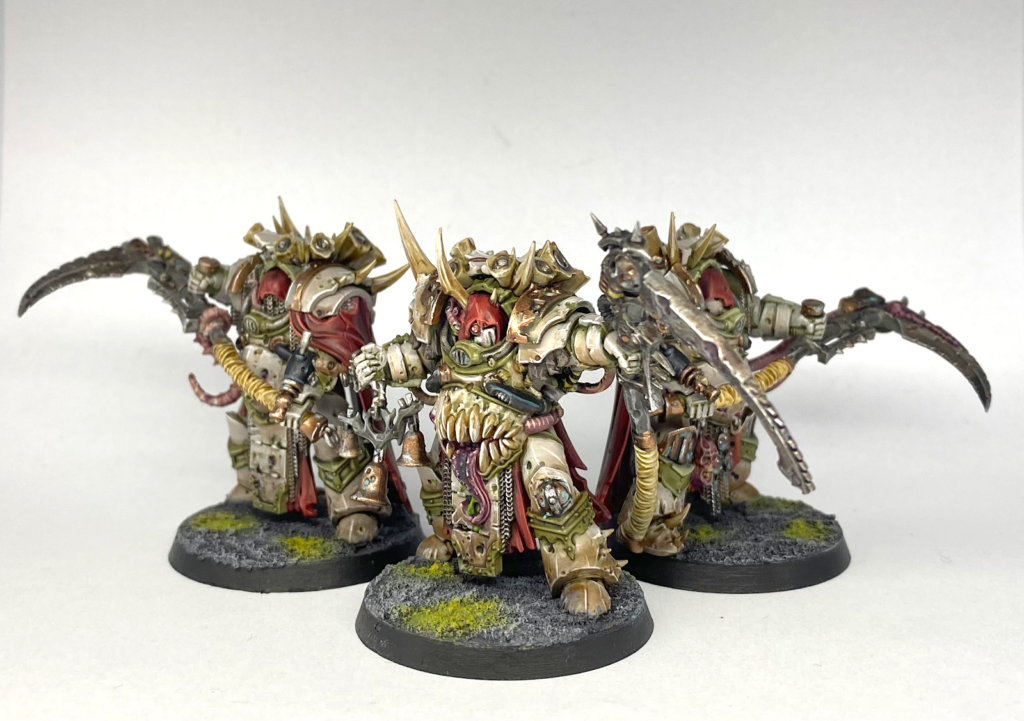 Photograph of three Deathshroud Terminator models, Heavily armoured space marines, they are covered in mutations and carry scythes. They are painted in bone white and wear red cowls and capes