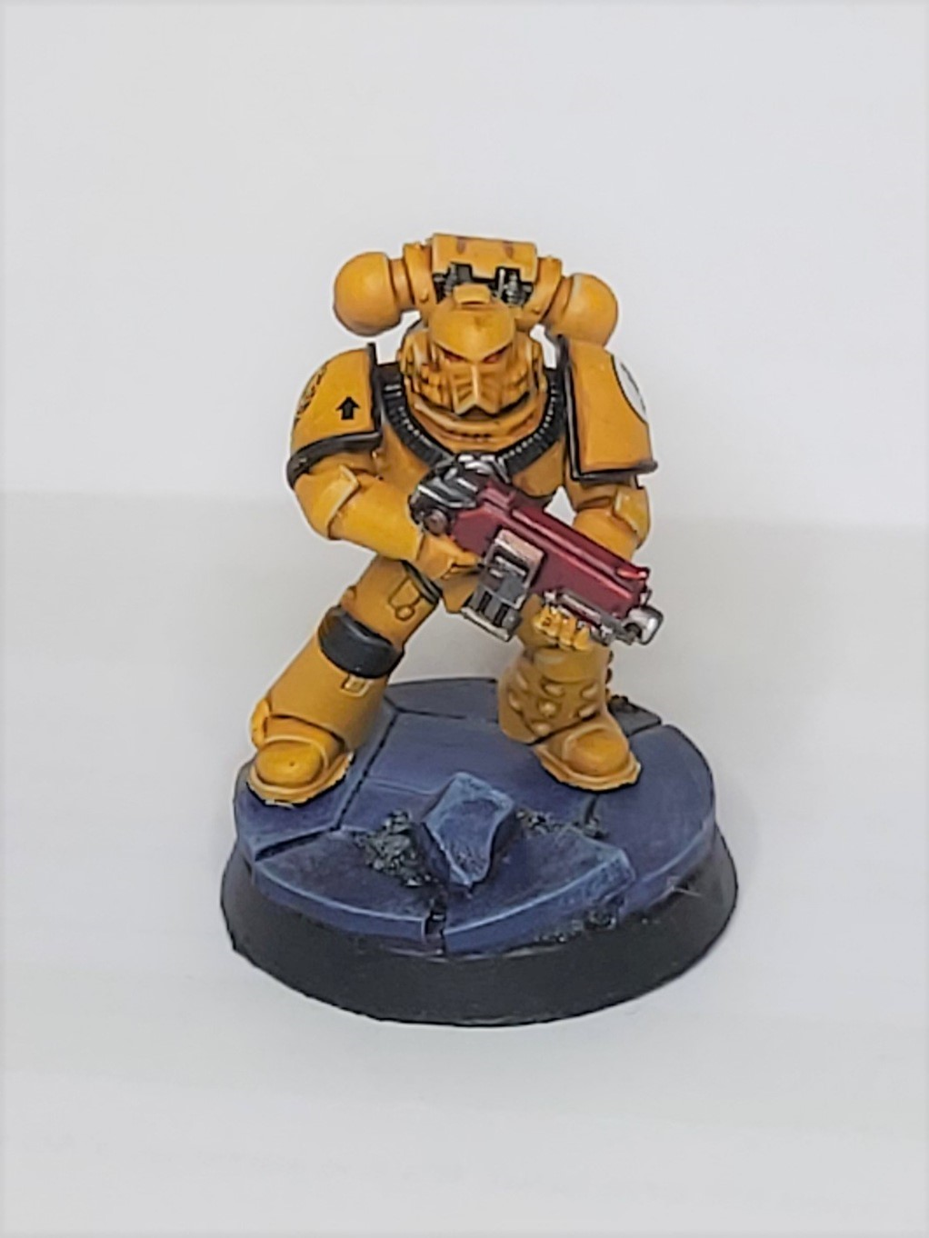 Model imperial fist, a space marine painted yellow and mounted on a sculpted base of blue rubble