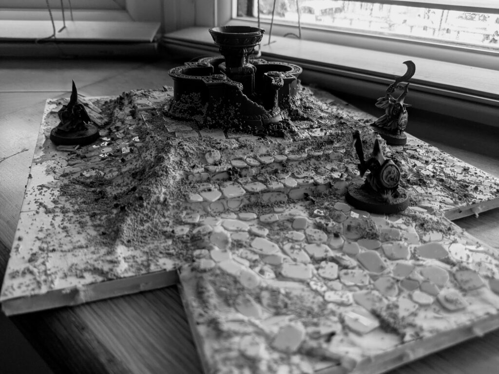 A black-and-white image of a terrain board, on a large squared base.