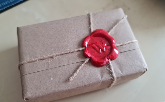 An image of small package wrapped neatly in brown paper and twine, with a wax seal. 
